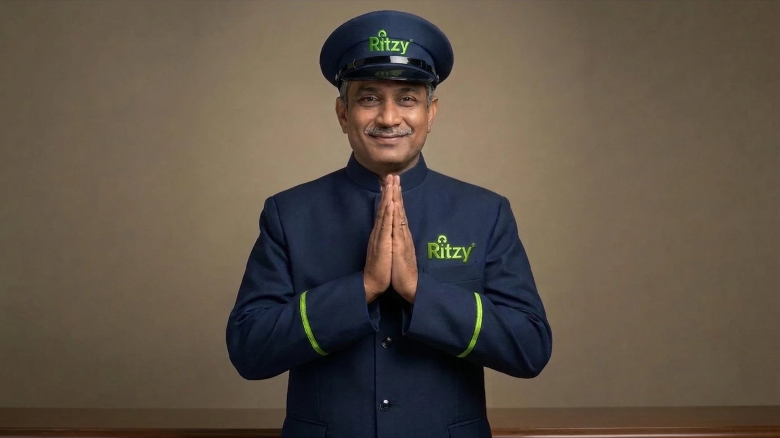 A Ritzy chauffeur in a navy uniform and cap greeting with a namaste